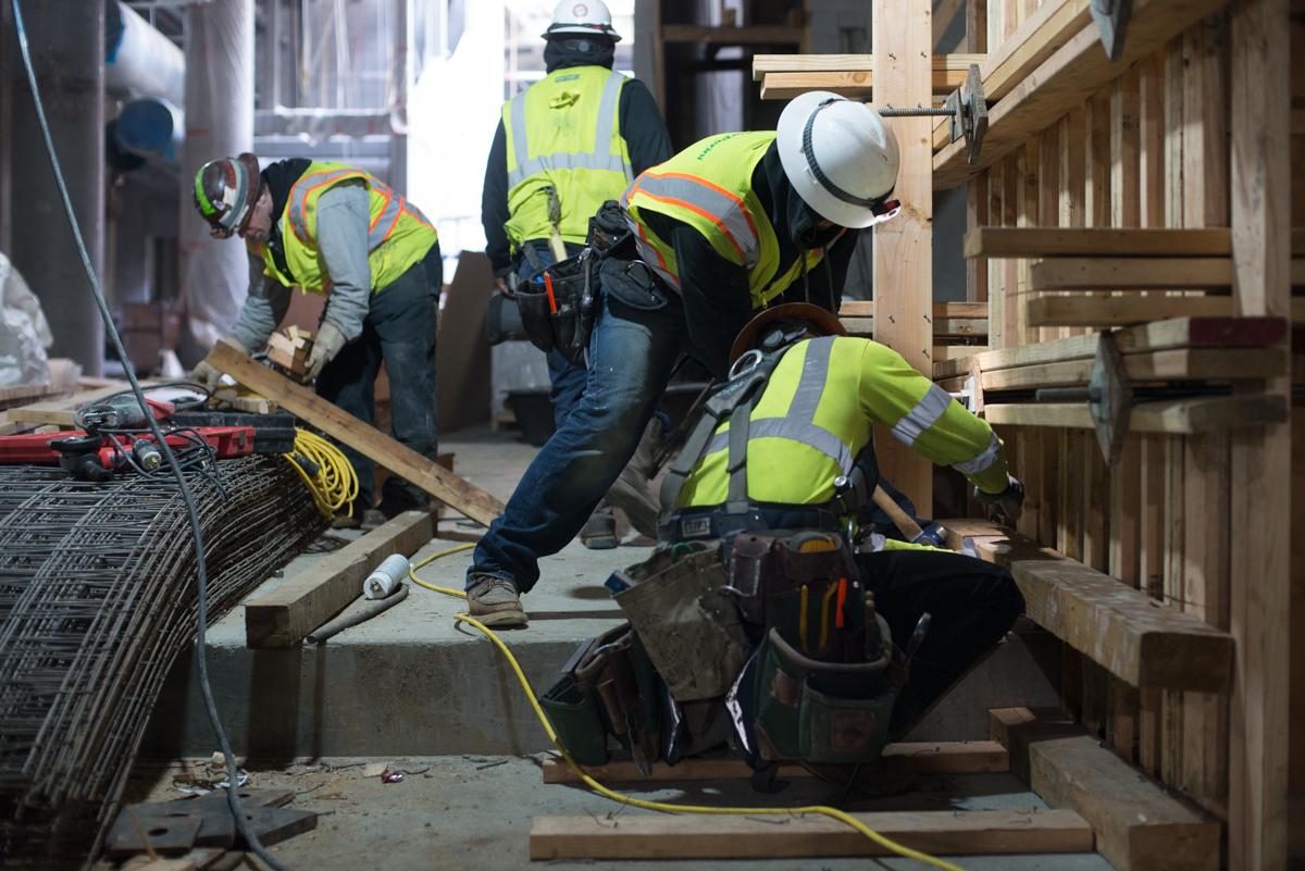 Construction workers in safety vests and hard hats install wooden forms and structural elements underground at a transit project site.