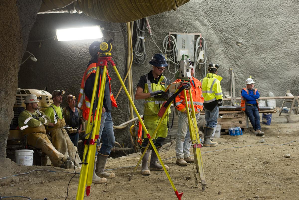 Construction workers with surveying equipment inside underground cavern excavation site.
