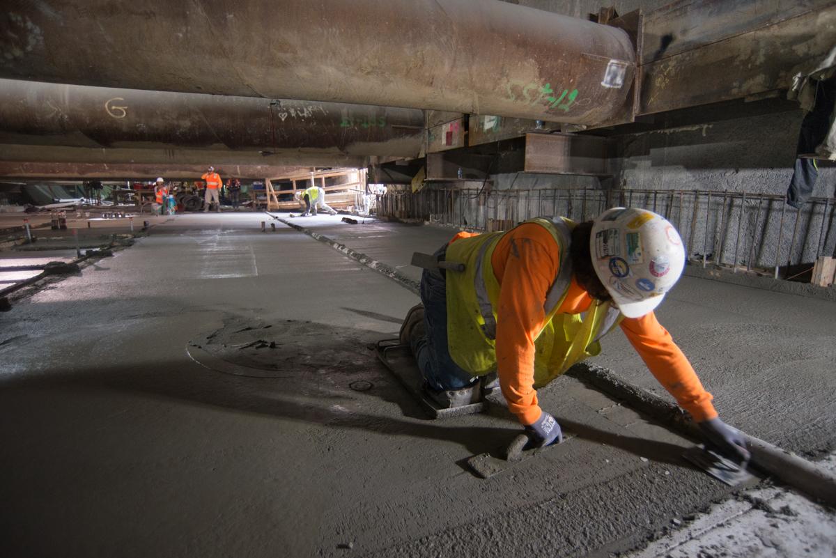 Worker in safety gear smoothing concrete floor inside underground transit station construction area.