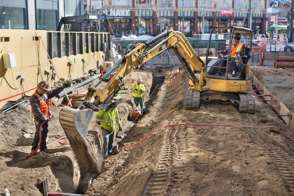 Construction crew operates excavator to install sewer pipes and utilities on 4th Street near Union Square.