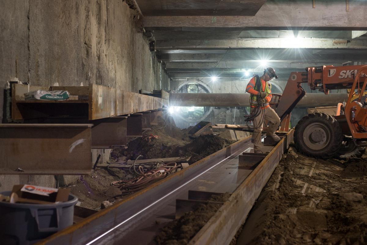 Workers install steel I-beam bracing inside underground transit station during construction.