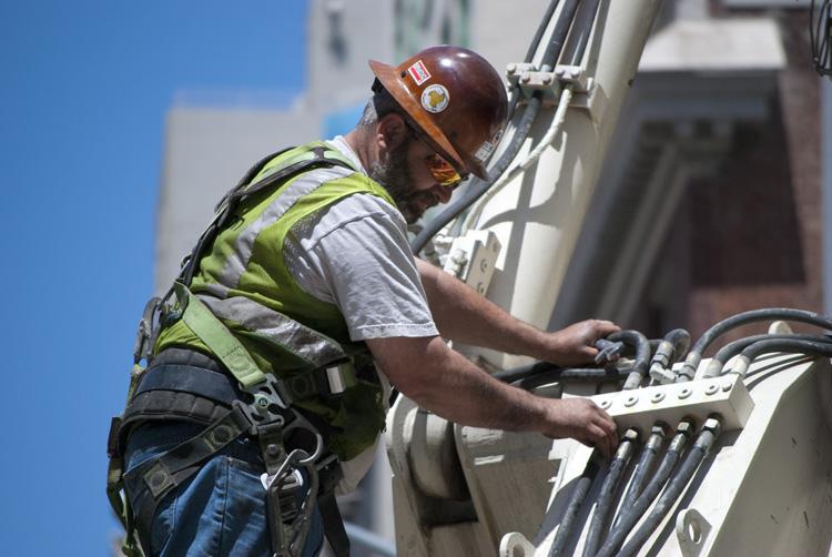 Worker in safety gear and hard hat performing maintenance on electrical equipment on building exterior.