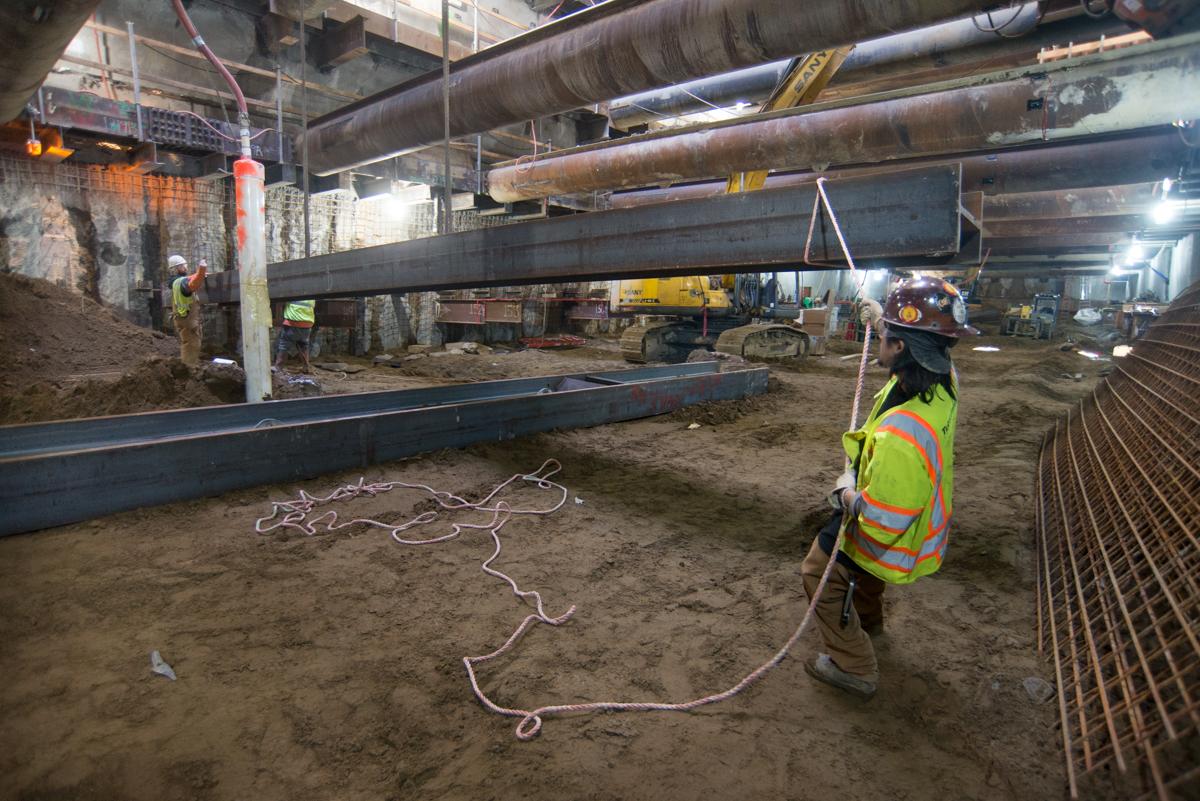 Construction worker in safety gear positioning steel beam at underground transit project site.