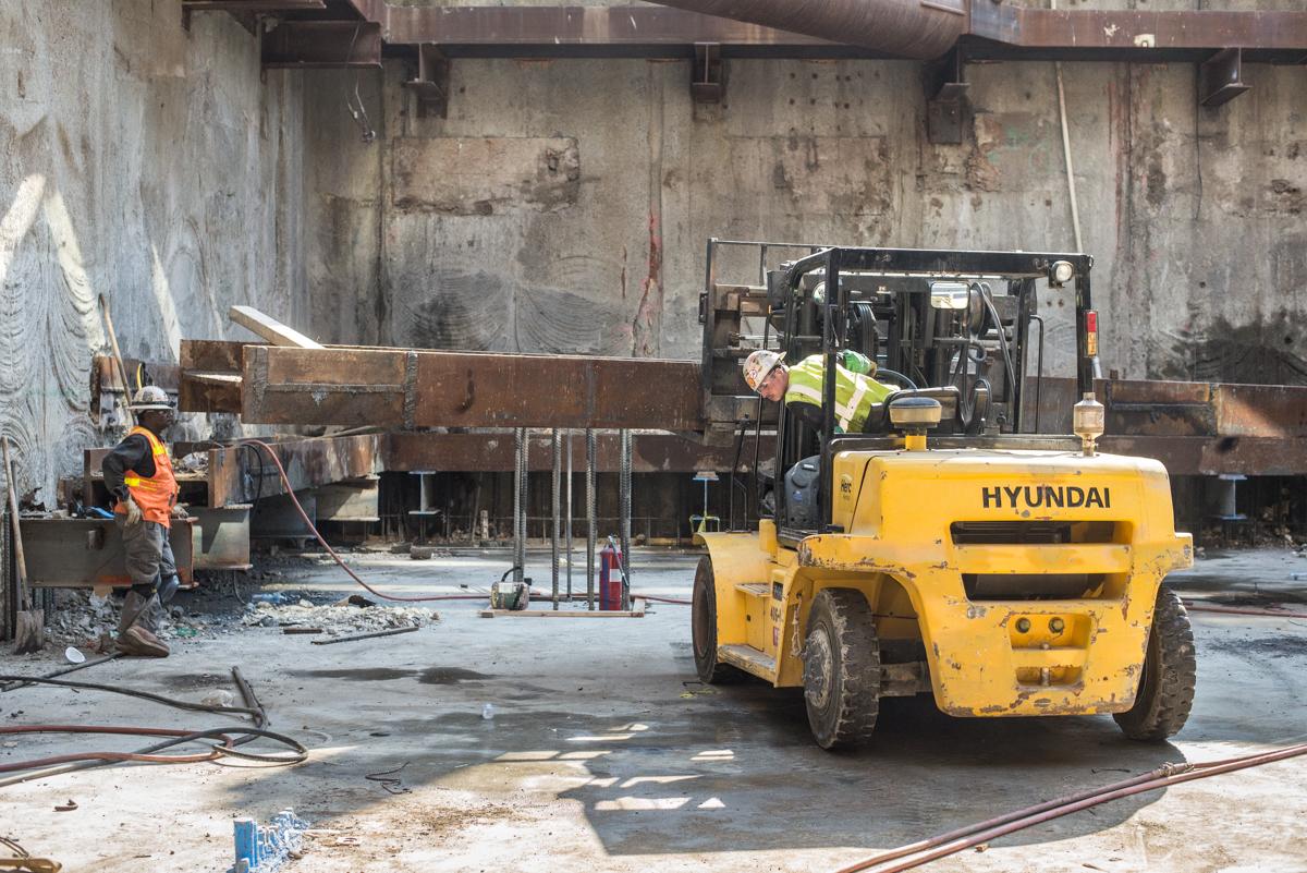 Yellow Hyundai forklift removing steel bracing from underground transit station construction site.