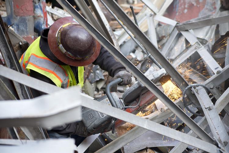 Worker in safety vest and hard hat inspecting metal structural framework at construction site.