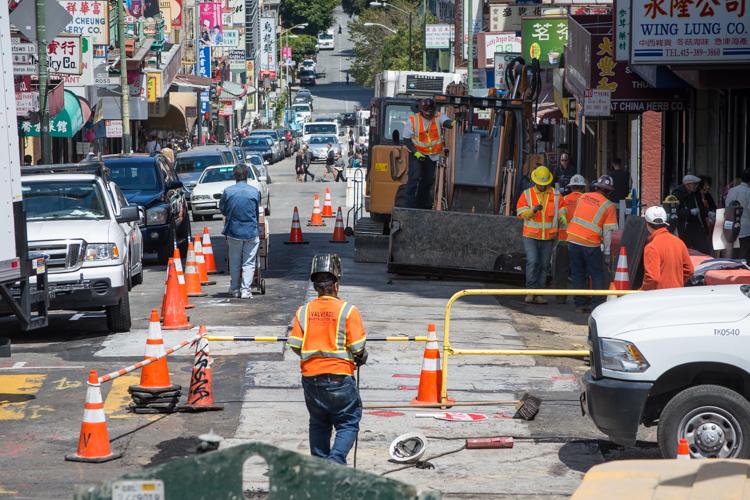 Workers in orange vests perform street maintenance on Washington Street, with traffic cones and equipment visible during lane closure.