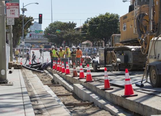 Construction workers and equipment on 4th Street with traffic cones and safety barriers blocking the roadway.