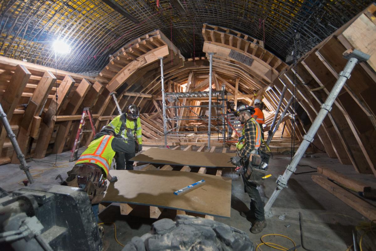 Workers in safety vests install concrete forms inside arched station entrance under construction.