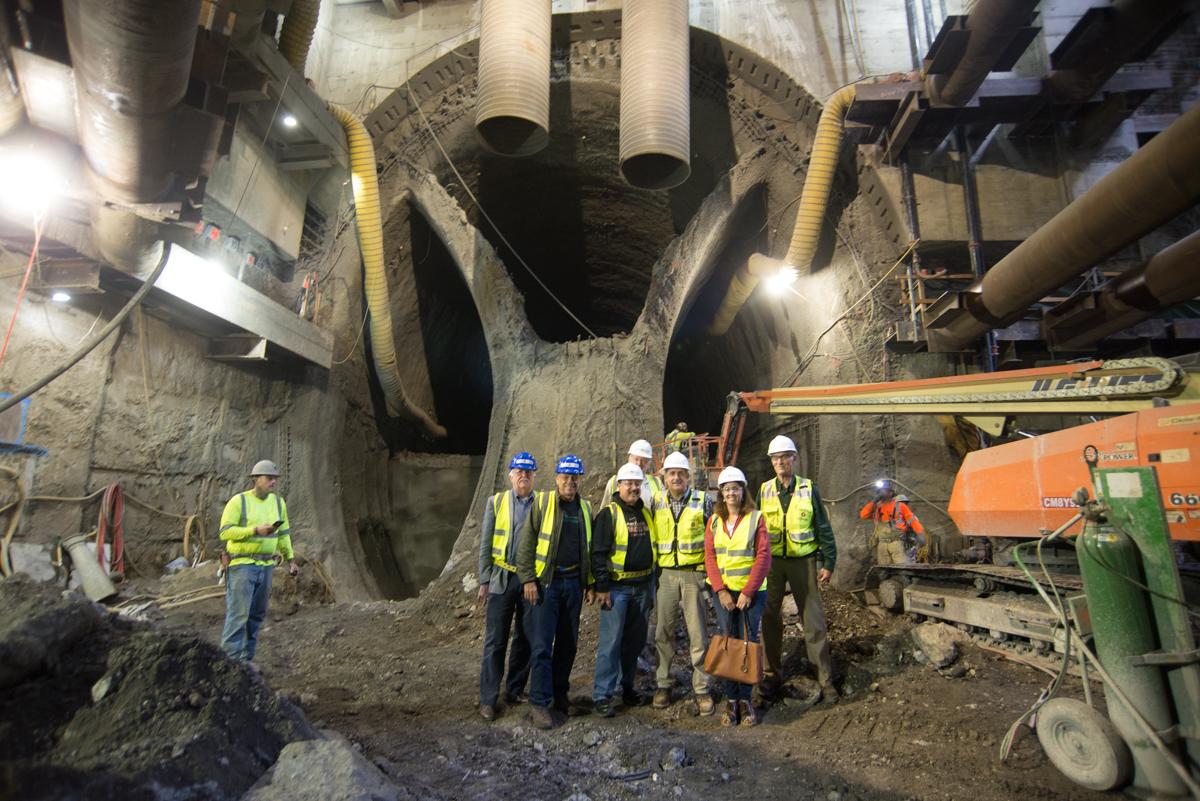 Construction workers in hard hats stand in front of large tunnel boring equipment at the Chinatown Station construction site.