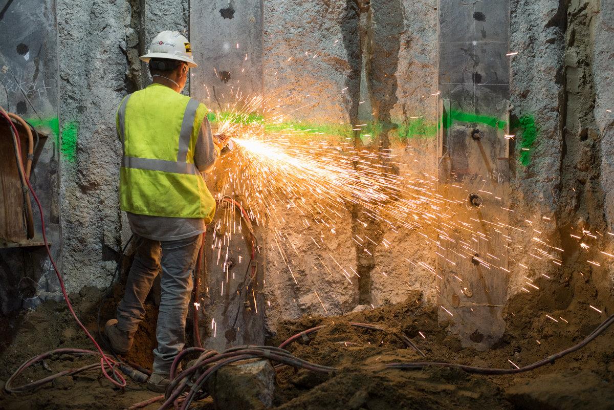 Worker in safety gear cutting steel with sparks flying on underground station construction site