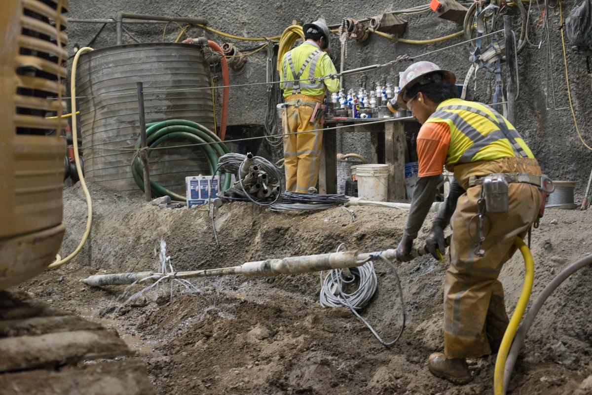 Workers in safety vests perform soil improvement work in underground station construction area.