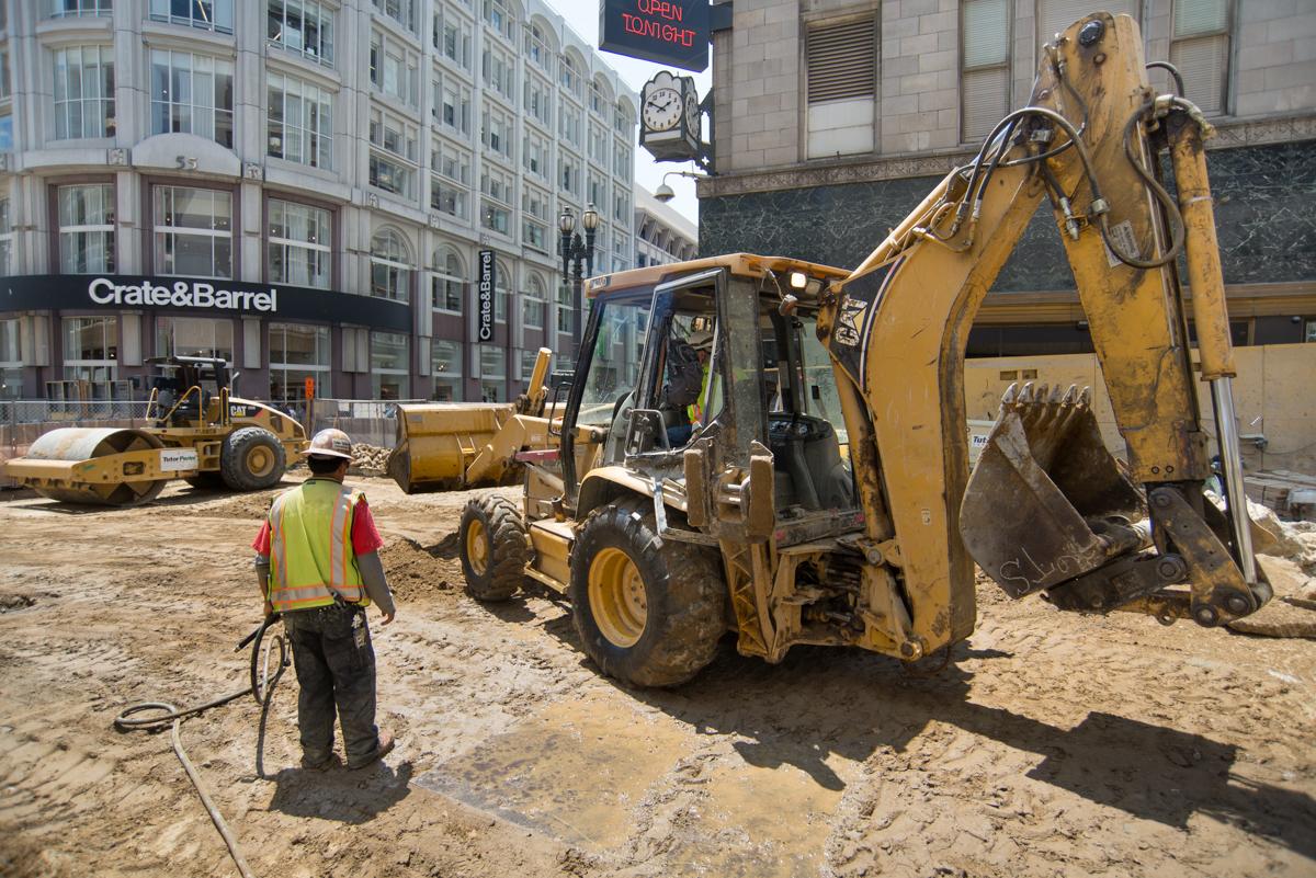 Construction worker in safety vest operating excavator with jackhammer at urban transit project site near Stockton Street.
