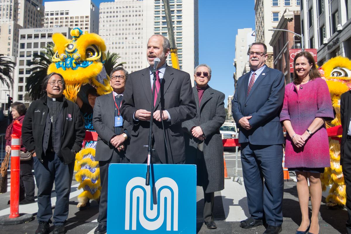 Officials and dignitaries at podium with lion dancers at urban transit celebration event.