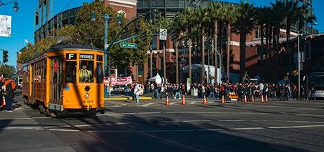 Yellow historic streetcar turning on Market Street with pedestrians and palm trees visible