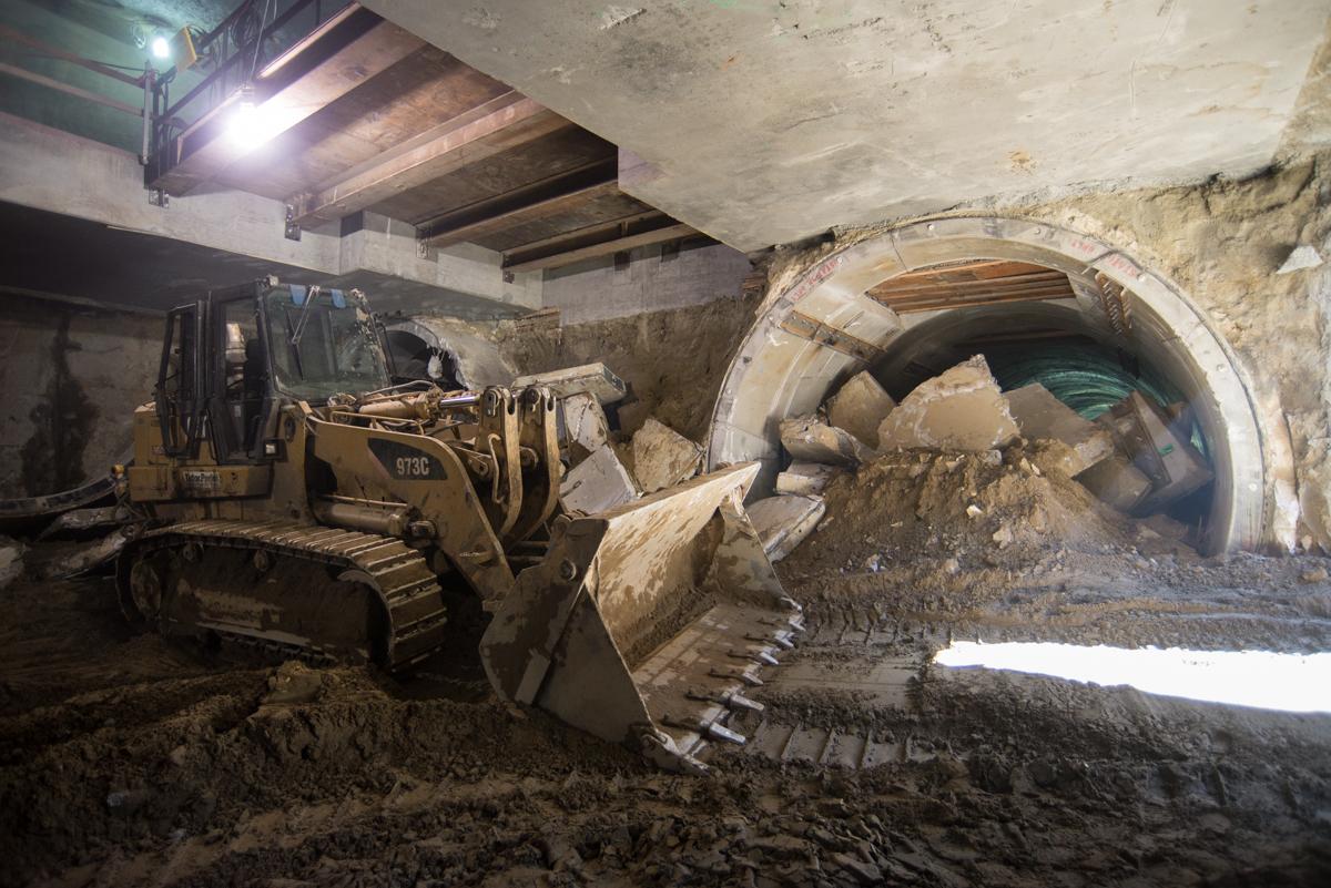 Bulldozer removing tunnel liner segments from underground station box during transit construction.