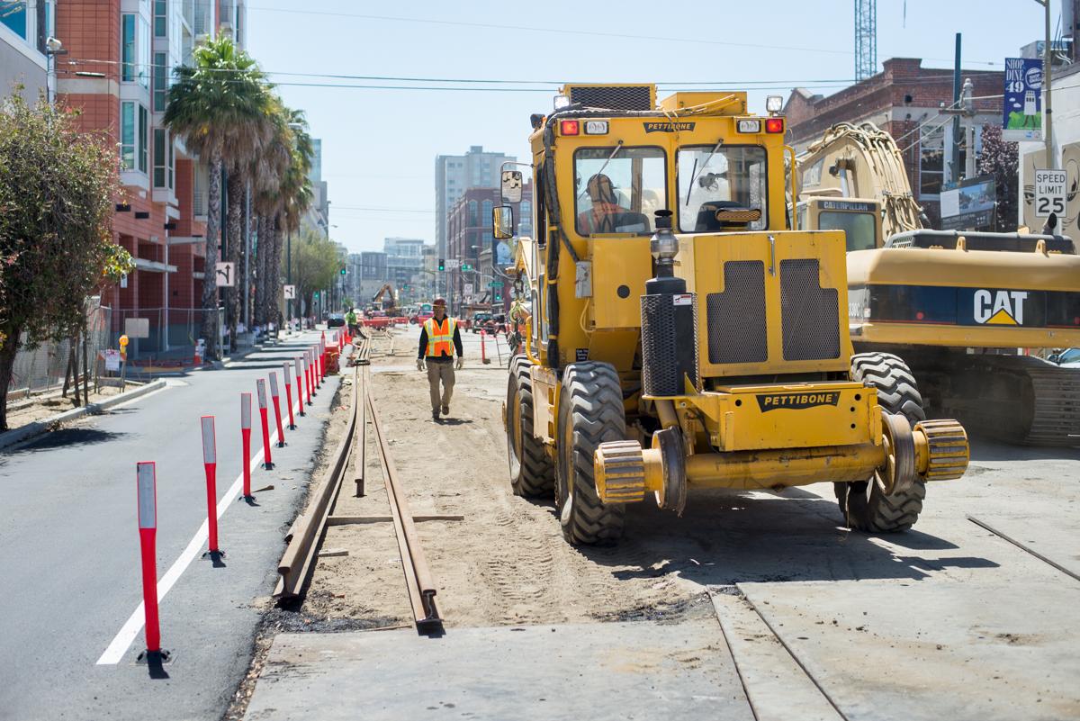 Construction equipment and workers on 4th Street installing transit rail infrastructure in an urban area.