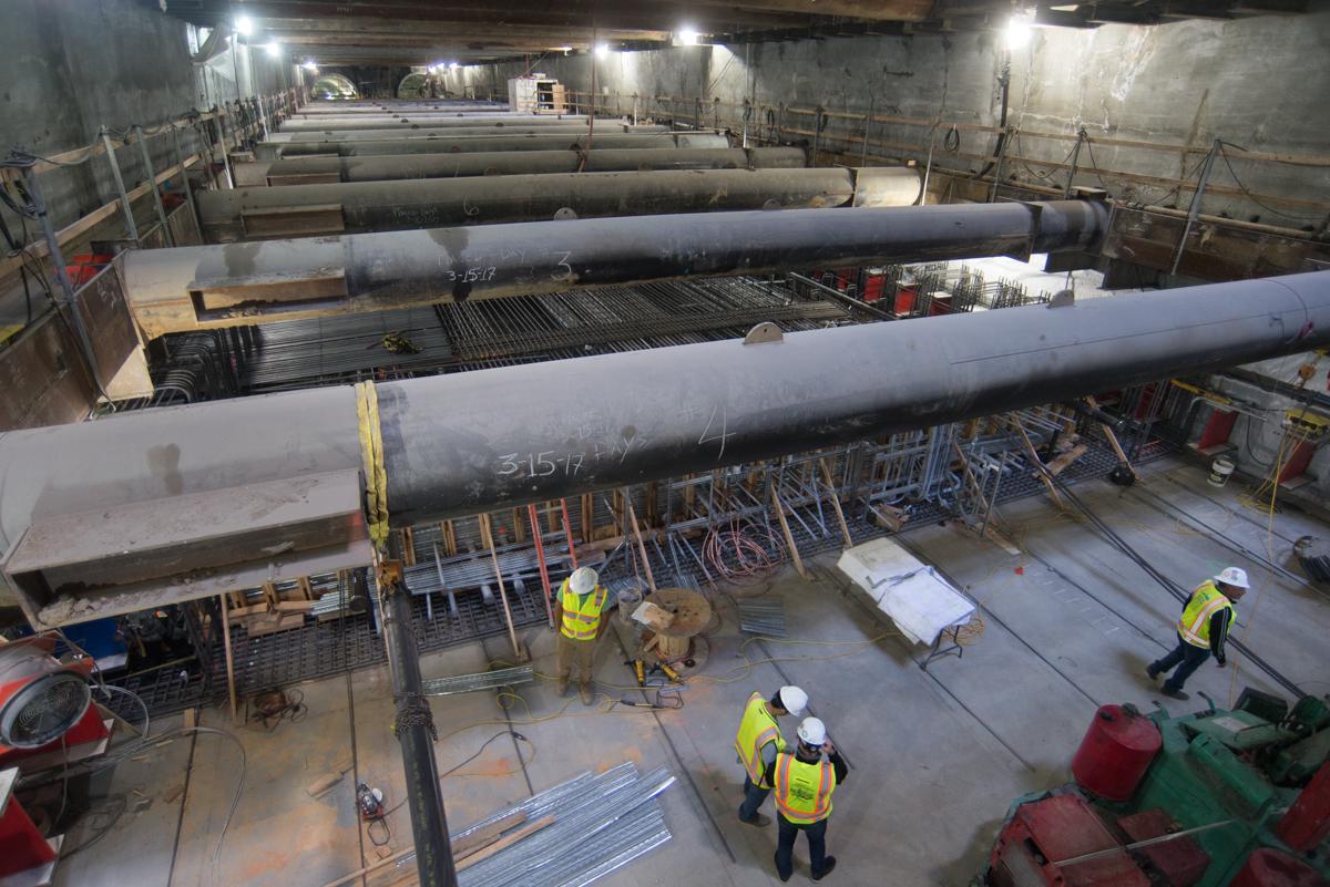 Large concrete tunnel sections under construction with workers in safety gear inside underground station excavation.
