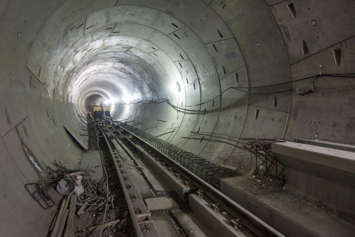 Underground tunnel with railway tracks and concrete walls lit by distant light source.