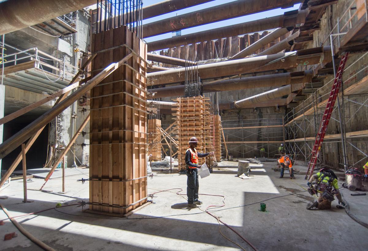 Construction workers assemble wooden formwork for concrete columns inside a transit station headhouse.