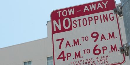Red and white tow-away zone sign showing no stopping times 7-9 a.m. and 4-6 p.m. weekdays, except holidays.