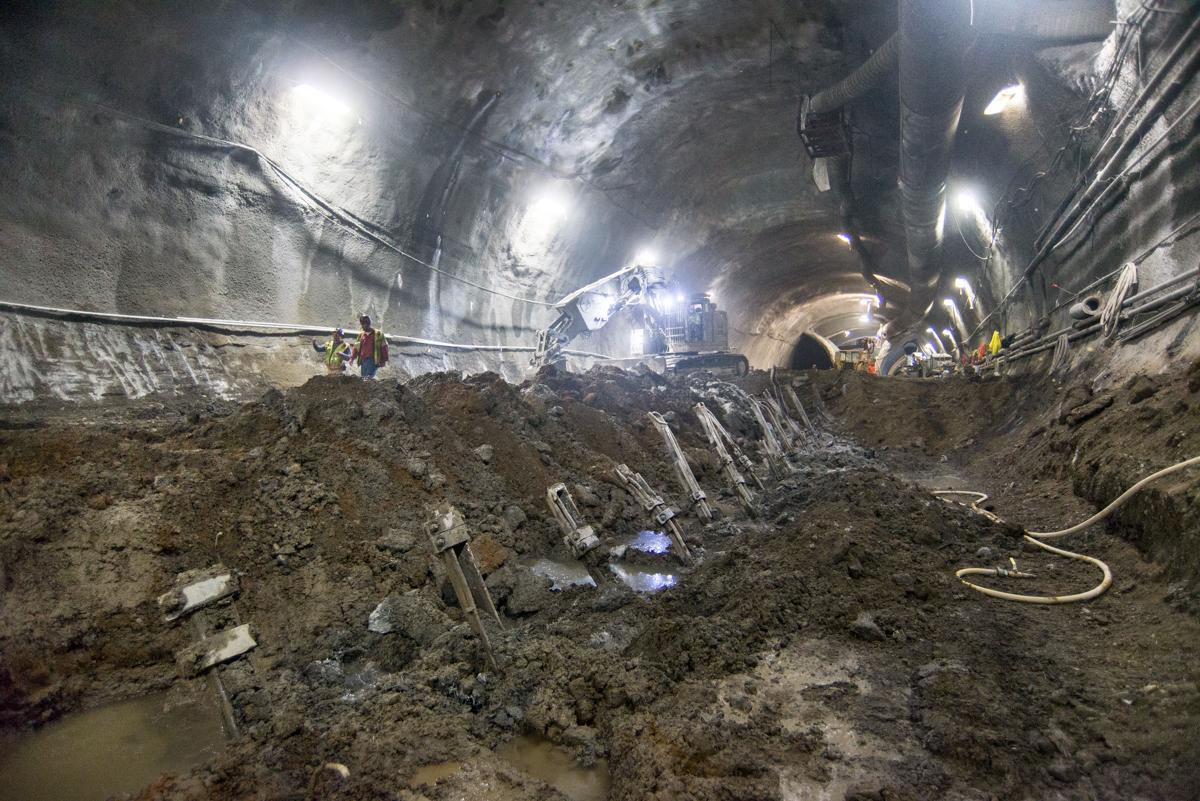 Underground tunnel construction site with exposed earth, steel reinforcement ribs, and work lighting.