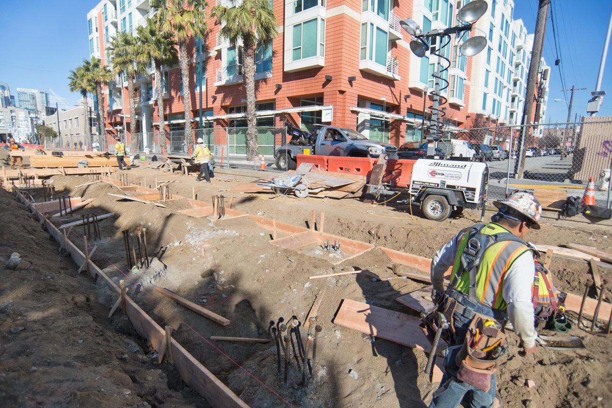 Construction workers in safety gear installing concrete forms and rebar for subway station foundation at 4th and Brannan.