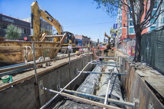 Construction site with excavator and underground utility pipes being installed on city street.