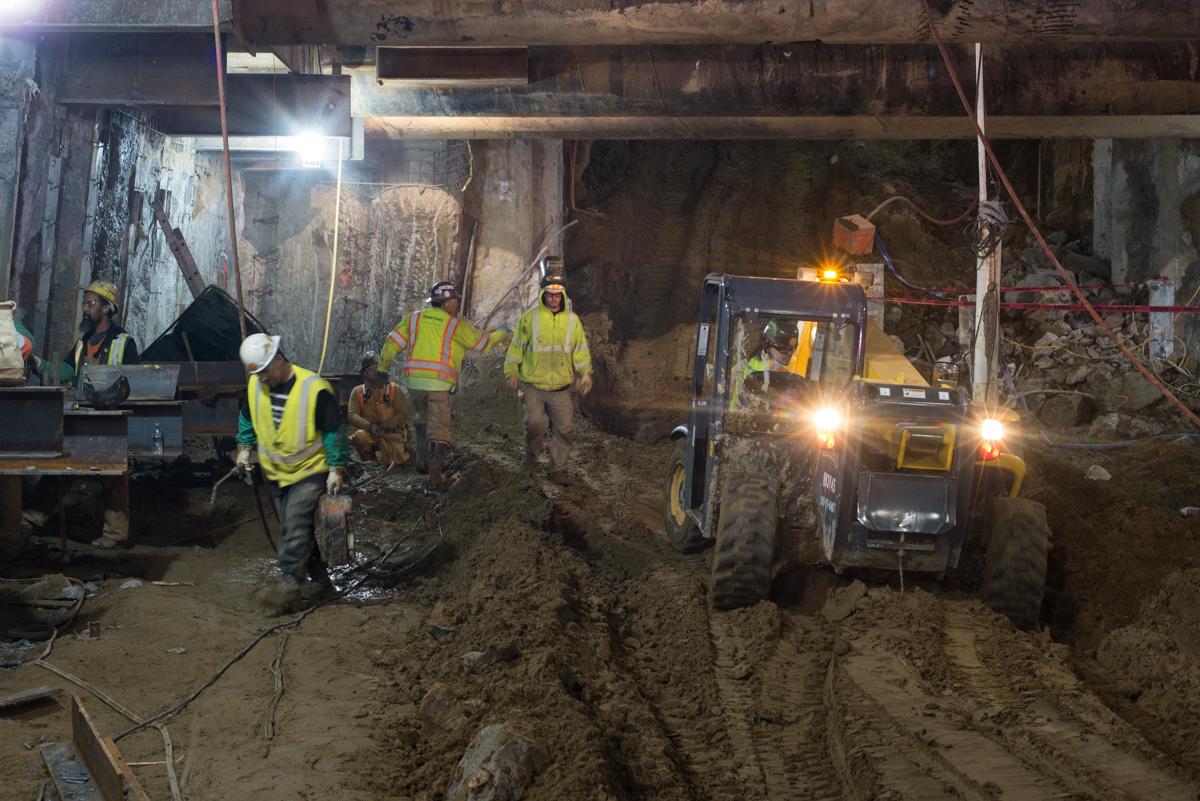 Workers in safety vests operate heavy equipment inside an underground construction site at night.