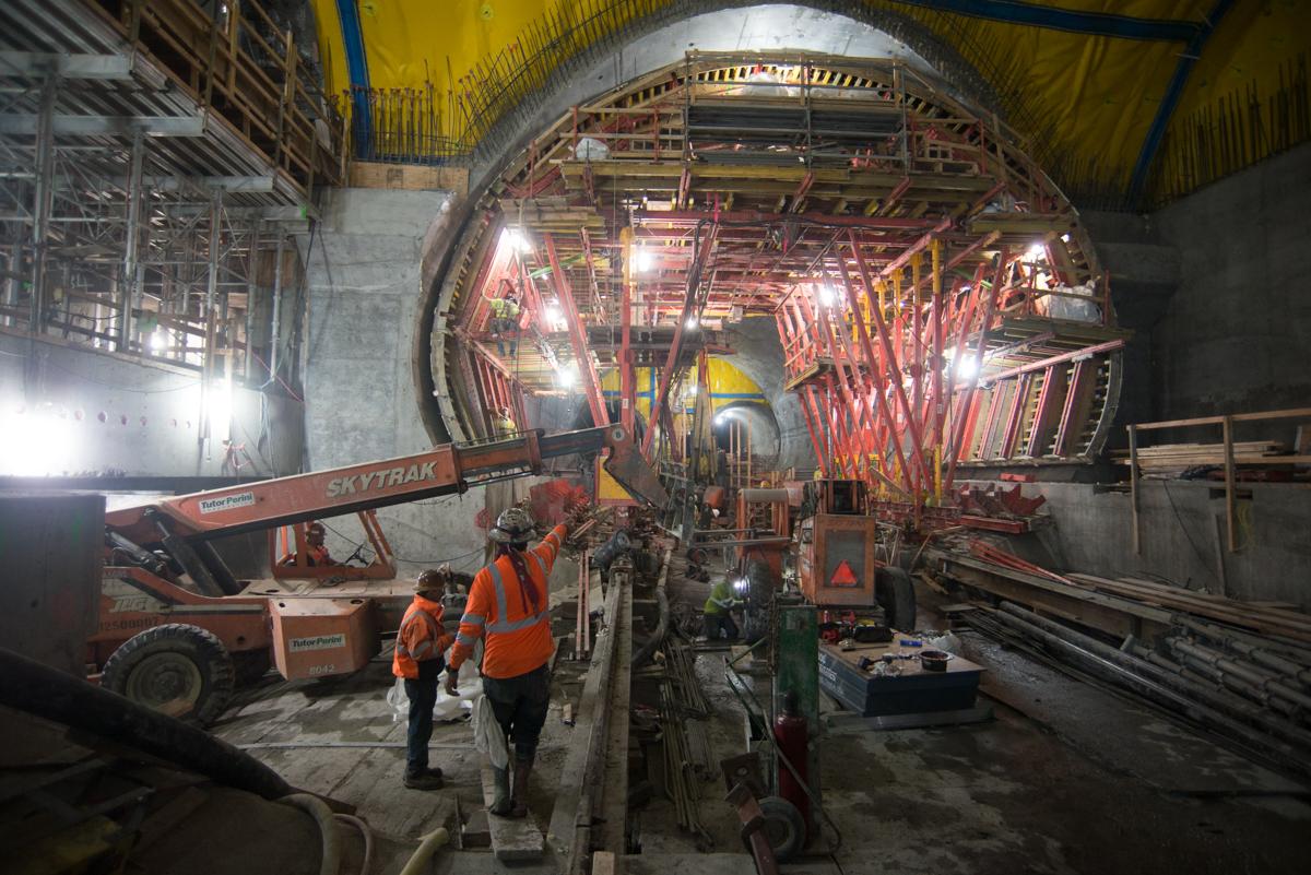 Workers in orange vests inside a tunnel with red support structures and construction equipment during transit infrastructure work.