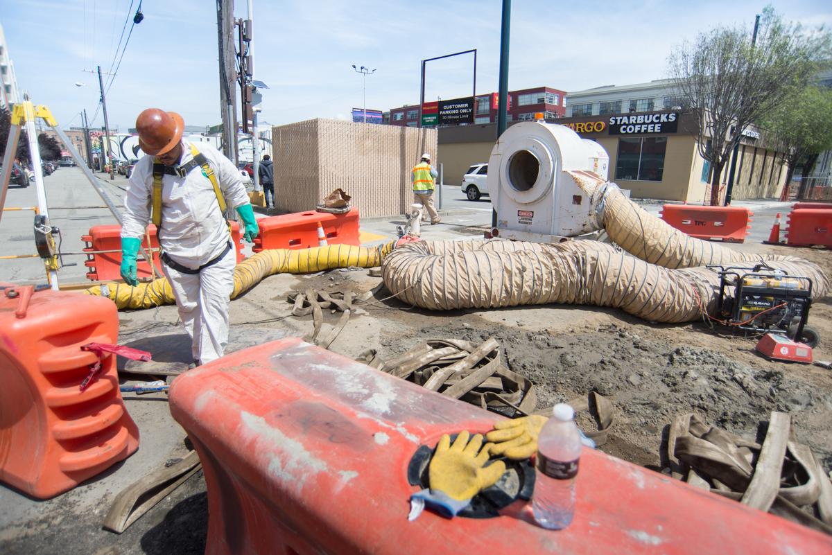 Workers in safety gear conduct sewer installation work on 4th Street with ventilation equipment and excavation barriers.