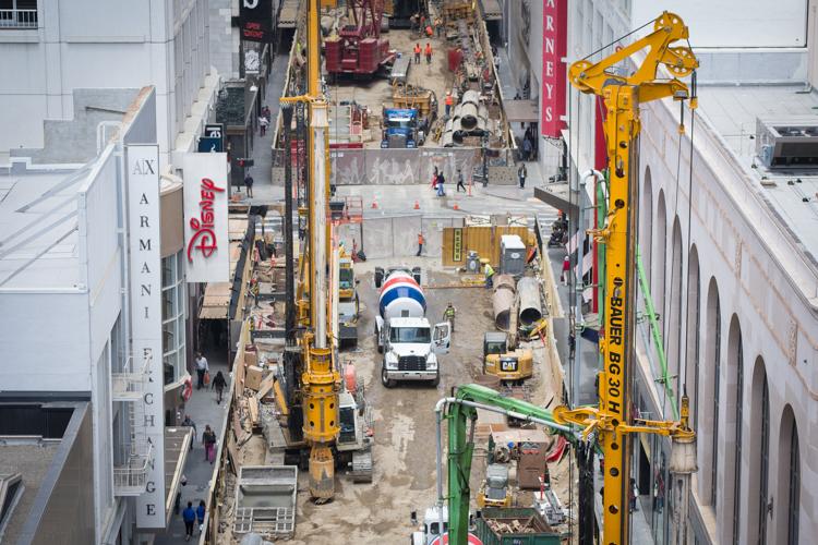 Aerial view of construction site on urban street with yellow cranes, concrete truck, equipment, and workers among surrounding buildings.