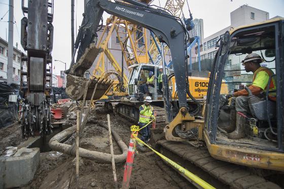Construction crew operates excavator on Ellis Street for underground utility work