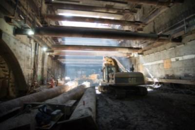 Construction excavation underway inside transit station headhouse with heavy equipment and exposed structural beams