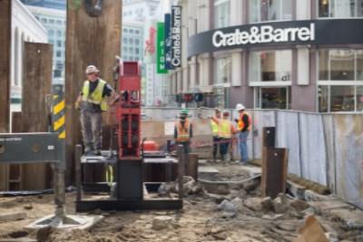 Construction workers in safety gear operate equipment at Union Square station renovation site near Crate&Barrel storefront.