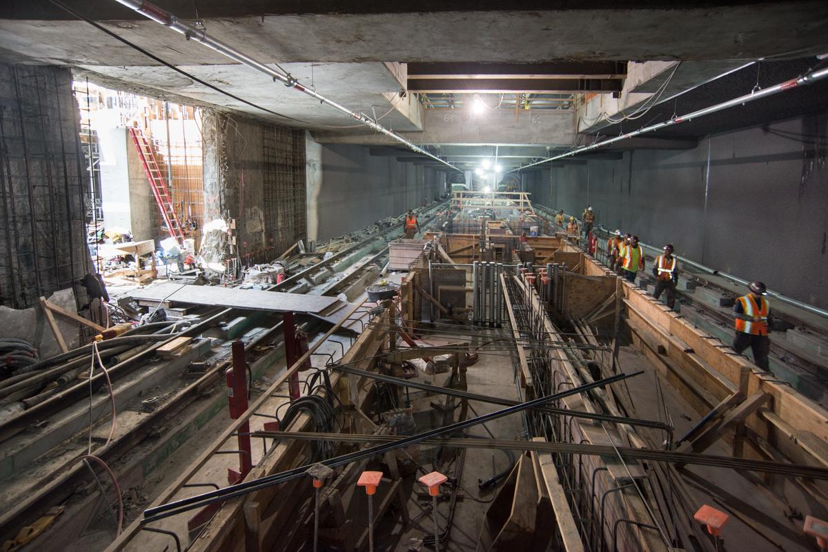 Workers and scaffolding inside underground transit station construction site with concrete forms and steel reinforcement visible.
