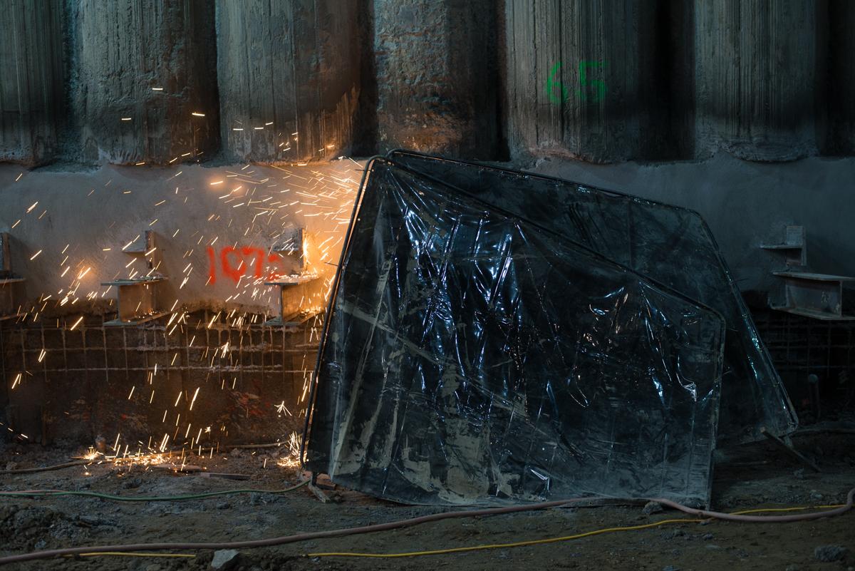Worker welding steel beam at underground transit station construction site with sparks flying.