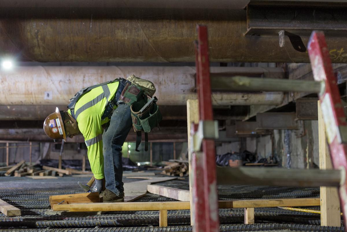 Worker in yellow safety vest bending over reinforced steel matting at underground station construction site.