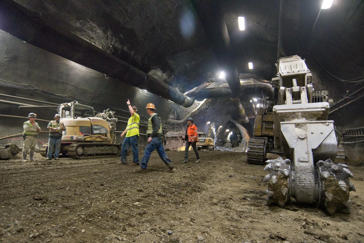 Workers and heavy equipment excavate underground station cavern at night under bright lighting.