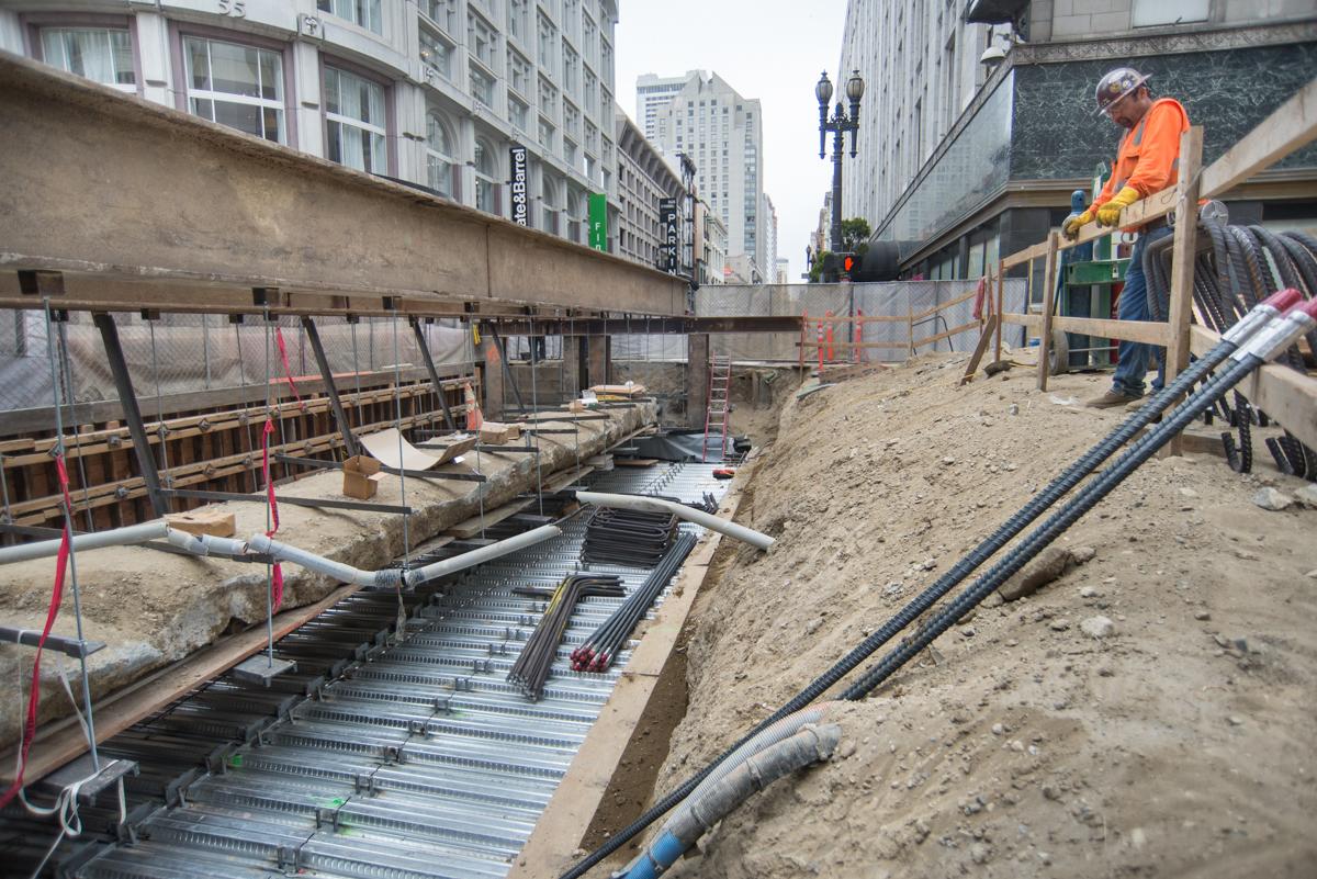 Construction site on O'Farrell Street with roof deck installation, excavation, and workers in safety gear.