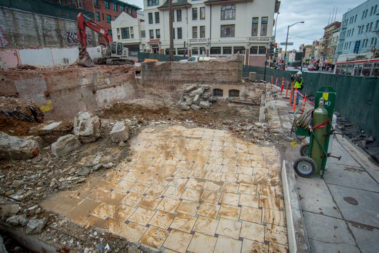 Construction site with excavated foundation, reinforced concrete base, and surrounding buildings in urban area.