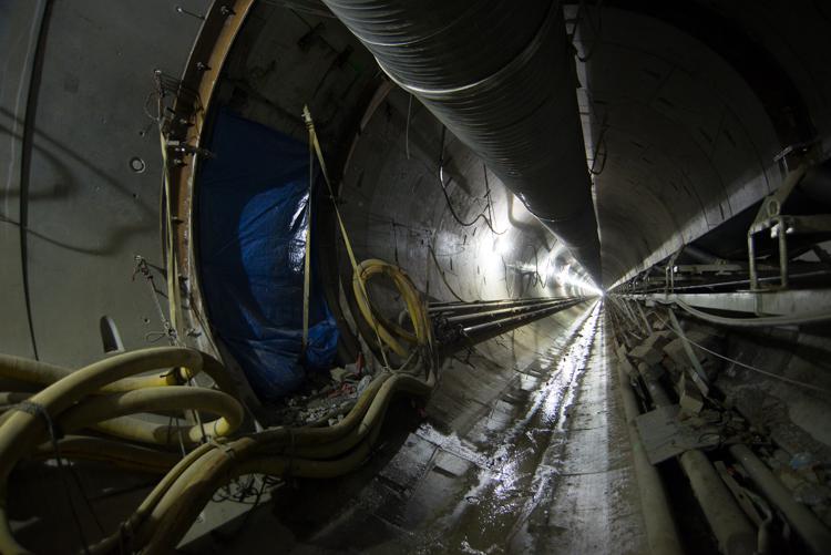 Tunnel cross-passage under construction connecting two parallel subway tunnels with blue tarp and yellow equipment visible.