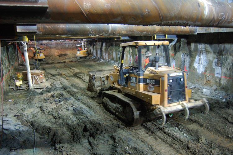 Excavation equipment operating inside underground tunnel construction site with support structures visible overhead.