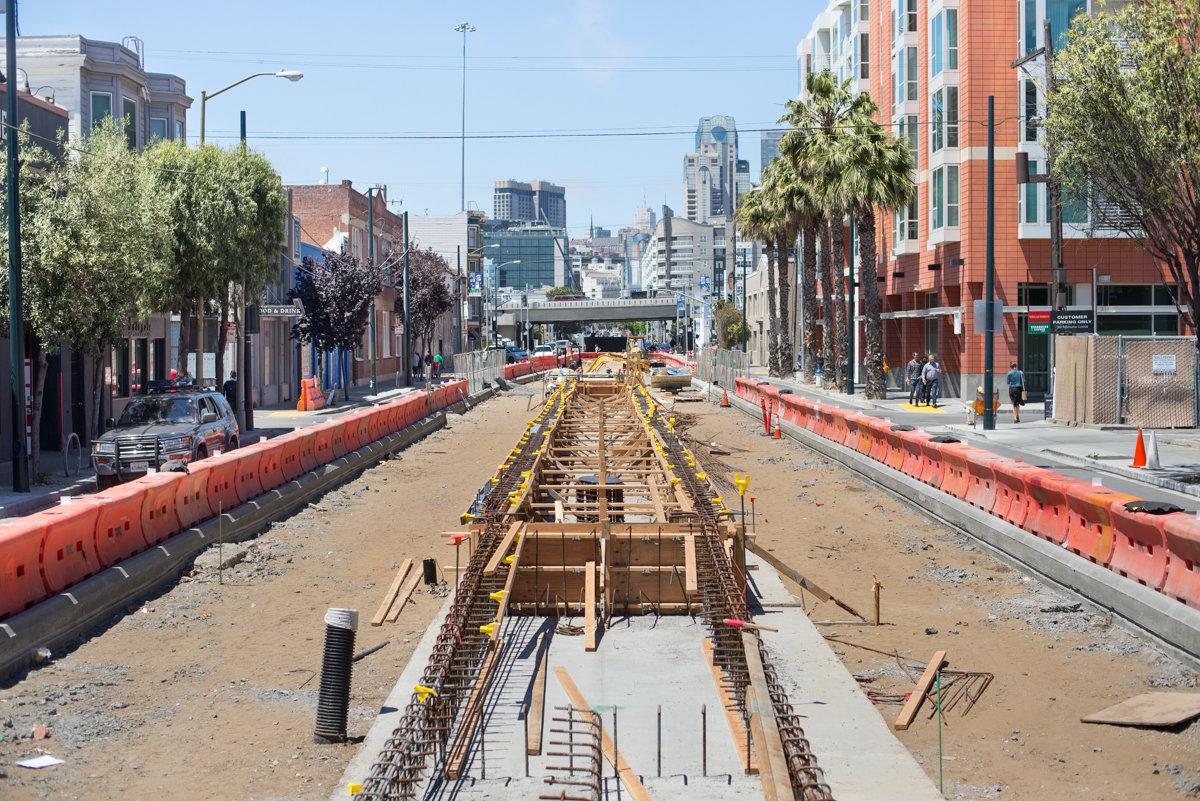 Construction site showing tunnel framework and concrete forms along Market Street subway project, with city skyline in background.