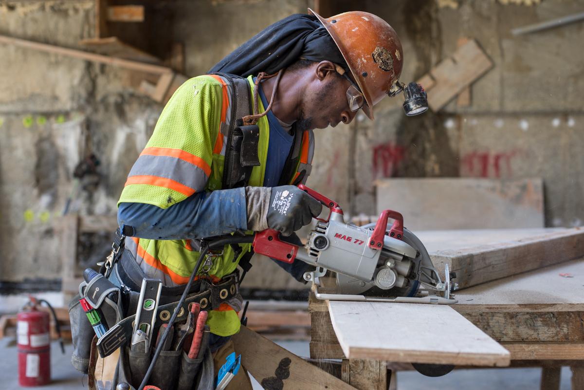 Construction worker using circular saw on wooden forms at underground transit station construction site.