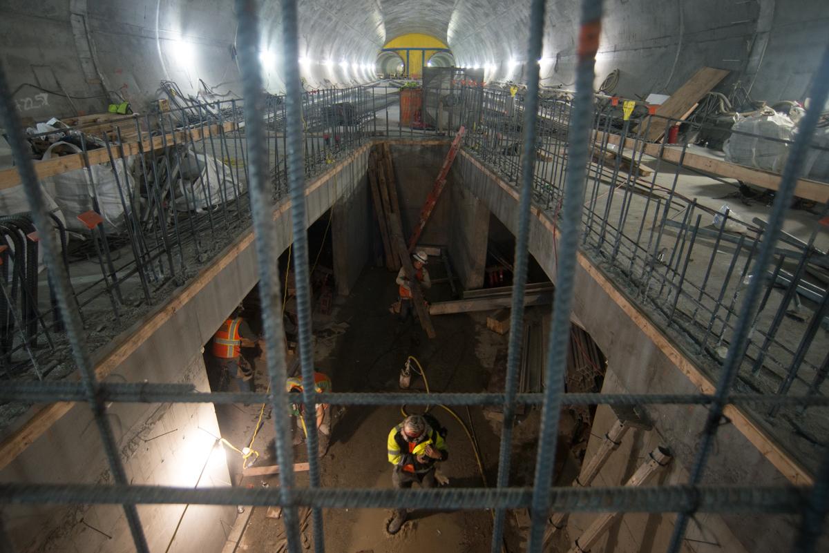Workers in safety gear construct underground tunnel section with concrete platform and metal scaffolding.