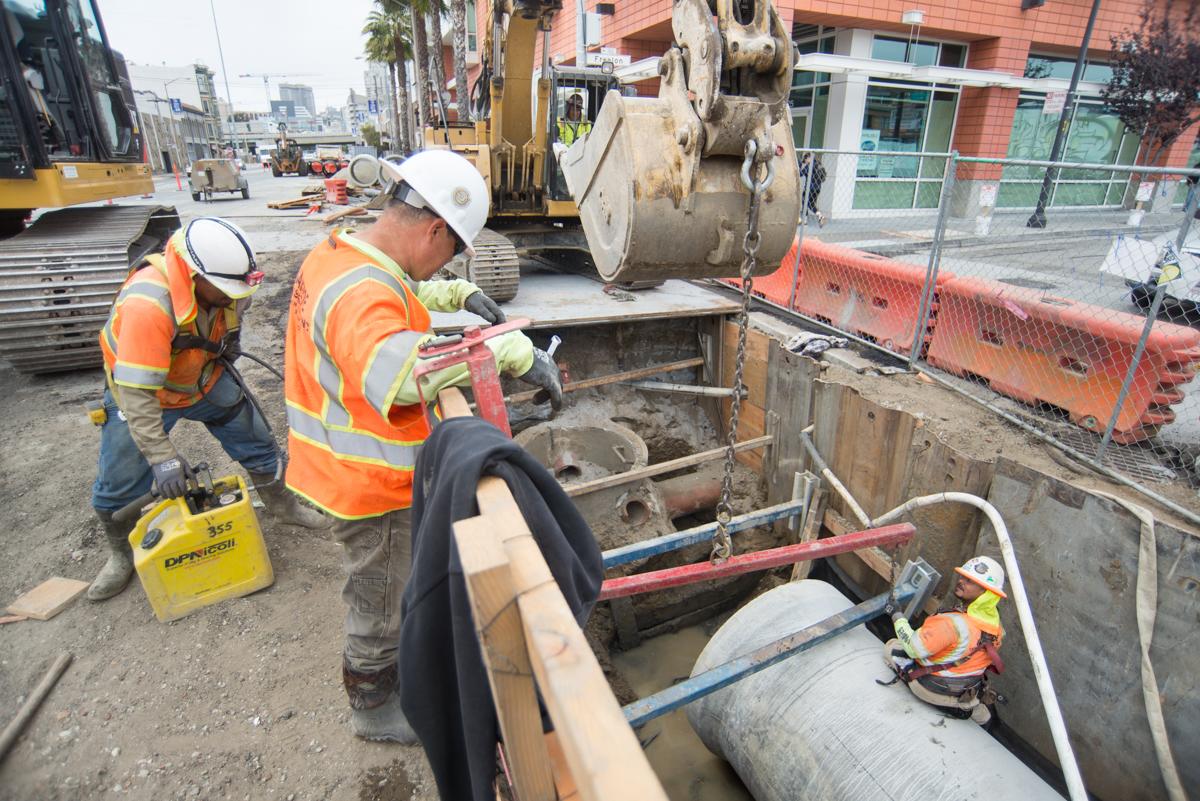 Construction workers install sewer lines in street trench at 4th and Freelon.