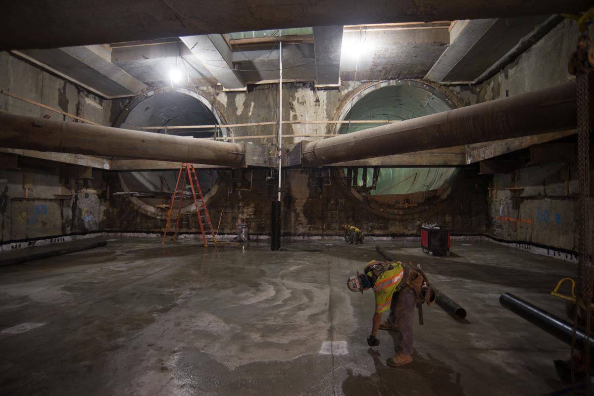 Worker in yellow safety vest inside underground transit station construction site with large circular tunnel sections.