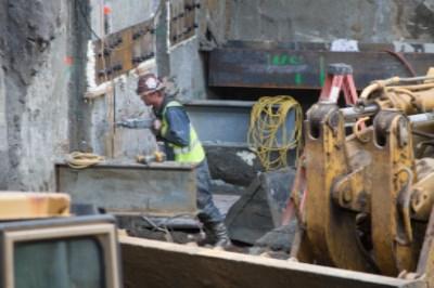 Worker in safety vest operating heavy machinery near station construction site with excavation equipment visible.