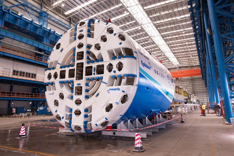 Blue and white tunnel boring machine with circular cutting head in industrial warehouse facility