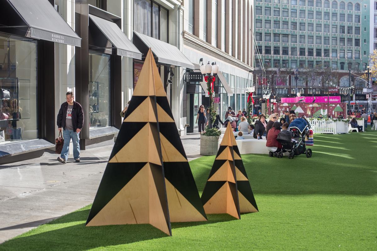 Stylized gold and black geometric trees decorate a pedestrian plaza during holiday festivities on Stockton Street.